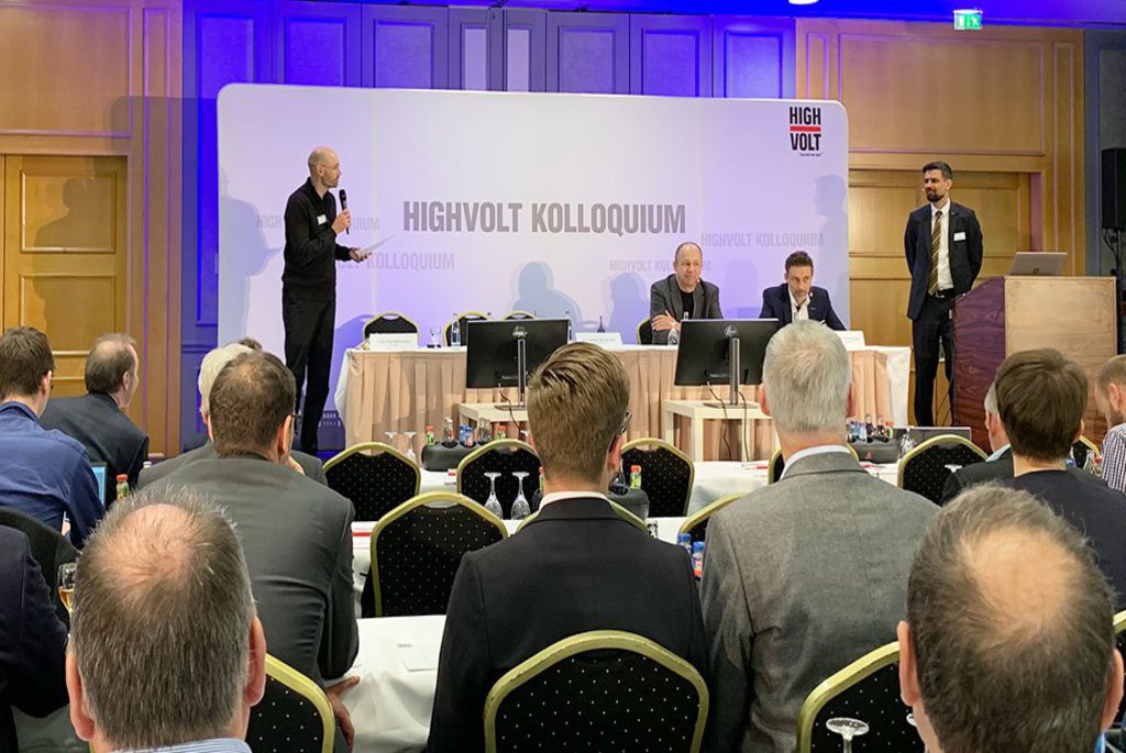 Ein Saal in dem mehrere Männer sitzen, im Hintergrund ist ein Pult zu sehen an dem ebenfalls Männer sitzen.