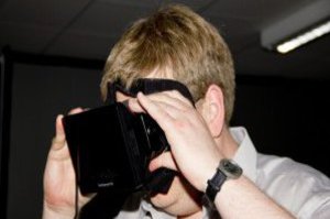 Ein Mann in grauem Hemd hält sich eine VR-Brille vor die Augen.