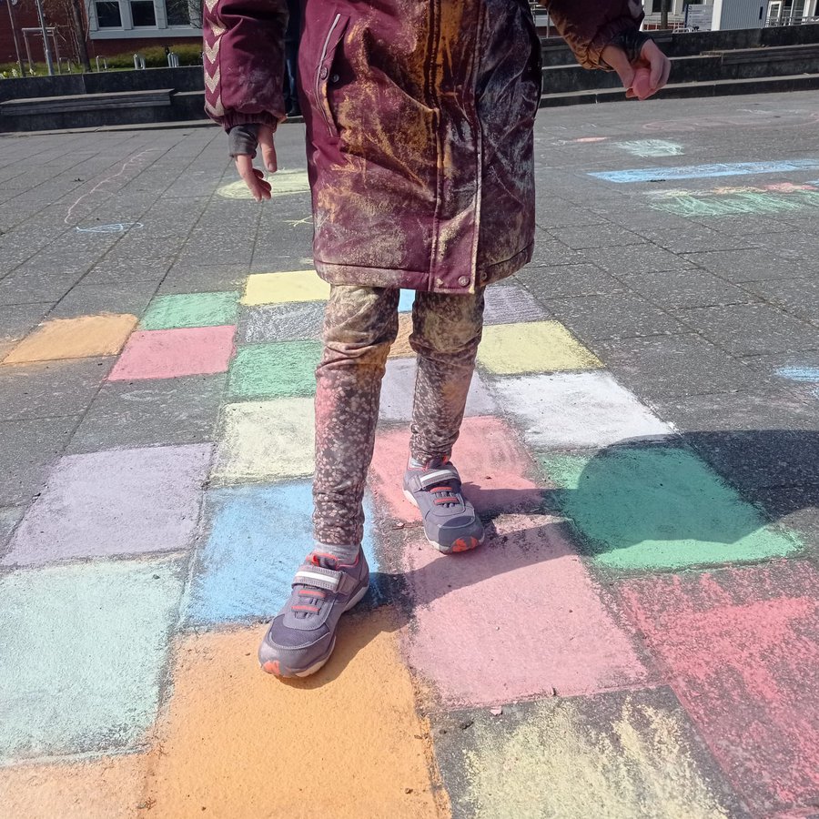 ein Kind steht auf einem mit Kreide auf das Pflaster gemalten Spielfeld