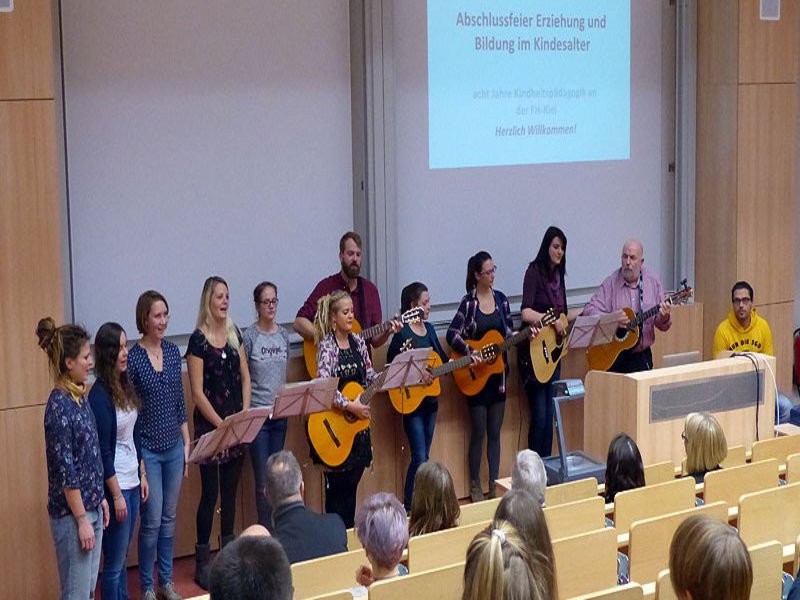 Eine Gruppe Musizierender steht mit Gitarren und Instrumenten in einem Hörsaal.