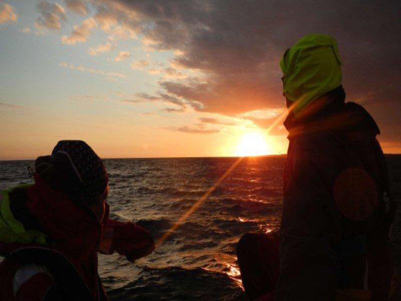 Zwei Männer segeln dem Sonnenuntergang entgegen.