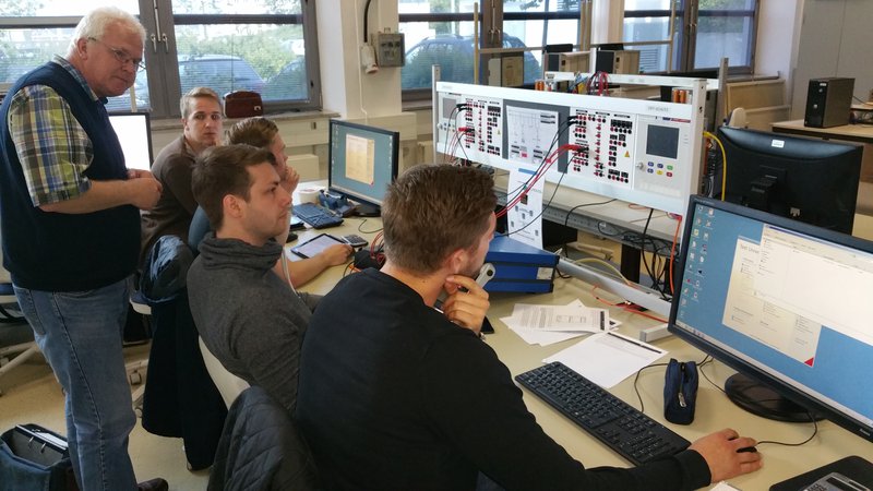 A picture of a Professor and his 4 students working in front of two monitors to interpret the values of a physical circuit