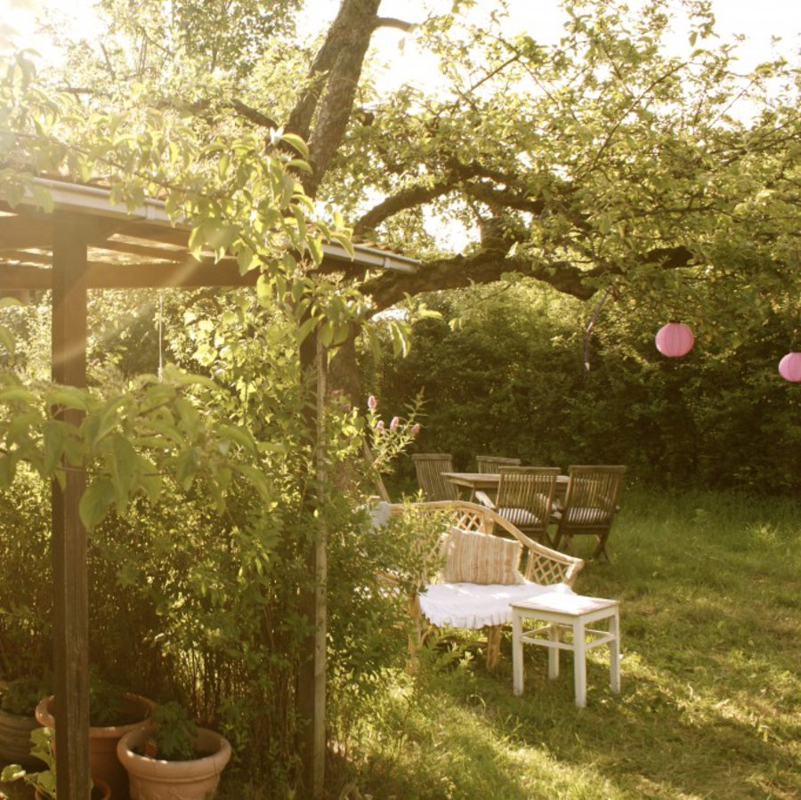 Ein schöner grüner Garten, mit einer gemütlichen Sitzecke und einem Balkendach.