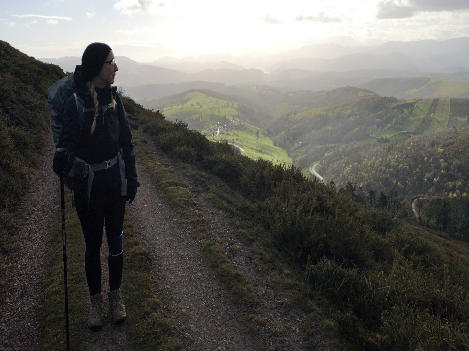 Eine Frau mit Wanderstock und Mütze marschiert auf dem Abhang eines Berges.