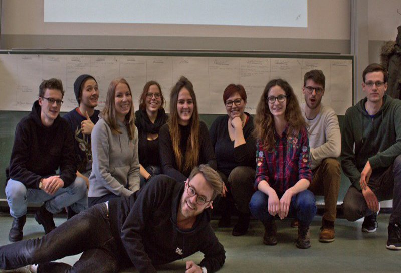 Eine Gruppe Studierender posiert vor einer Leinwand.