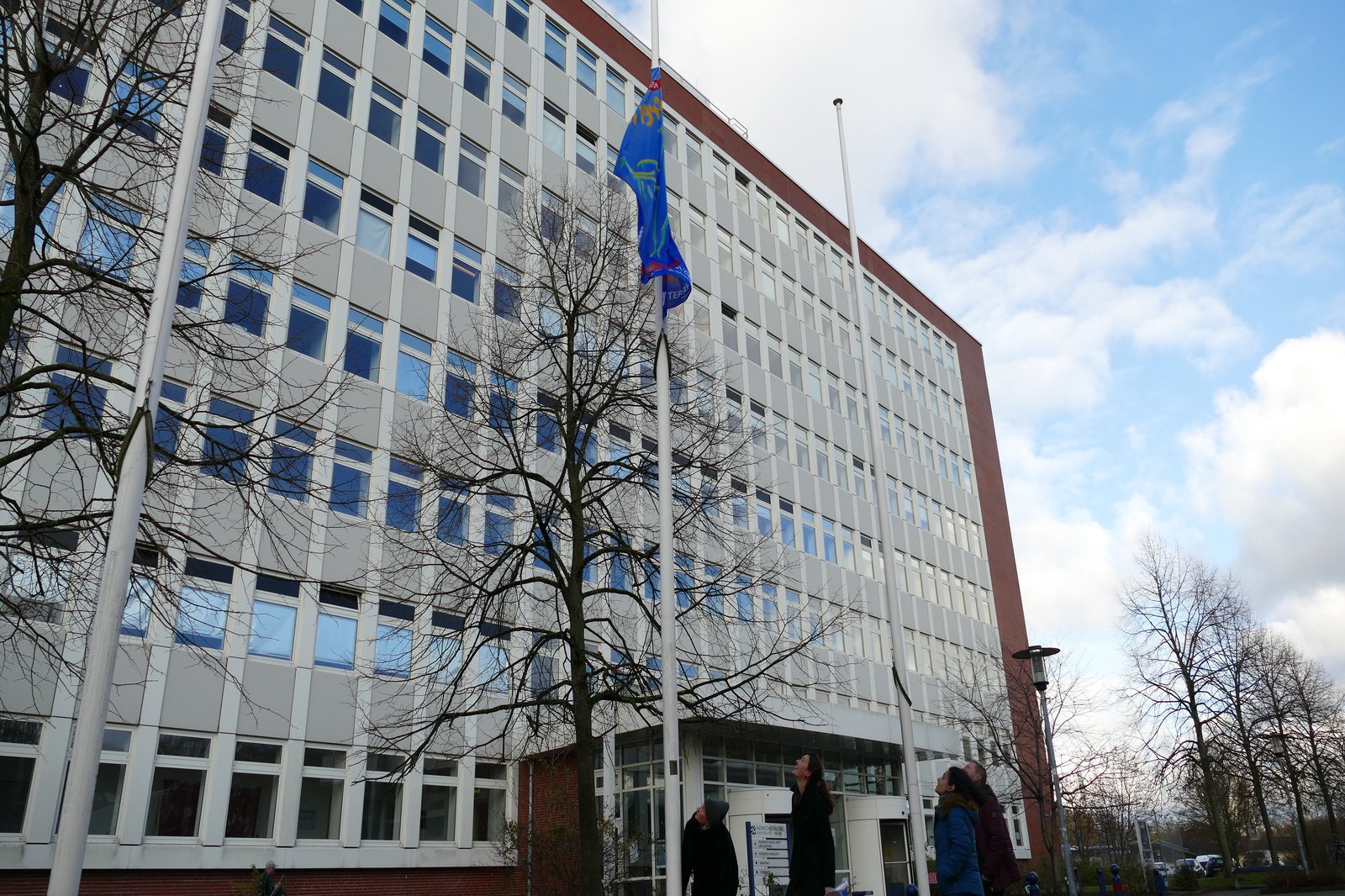 Eine auf Halbmast hängende blaue Fahne vor einem weissen Gebäude.