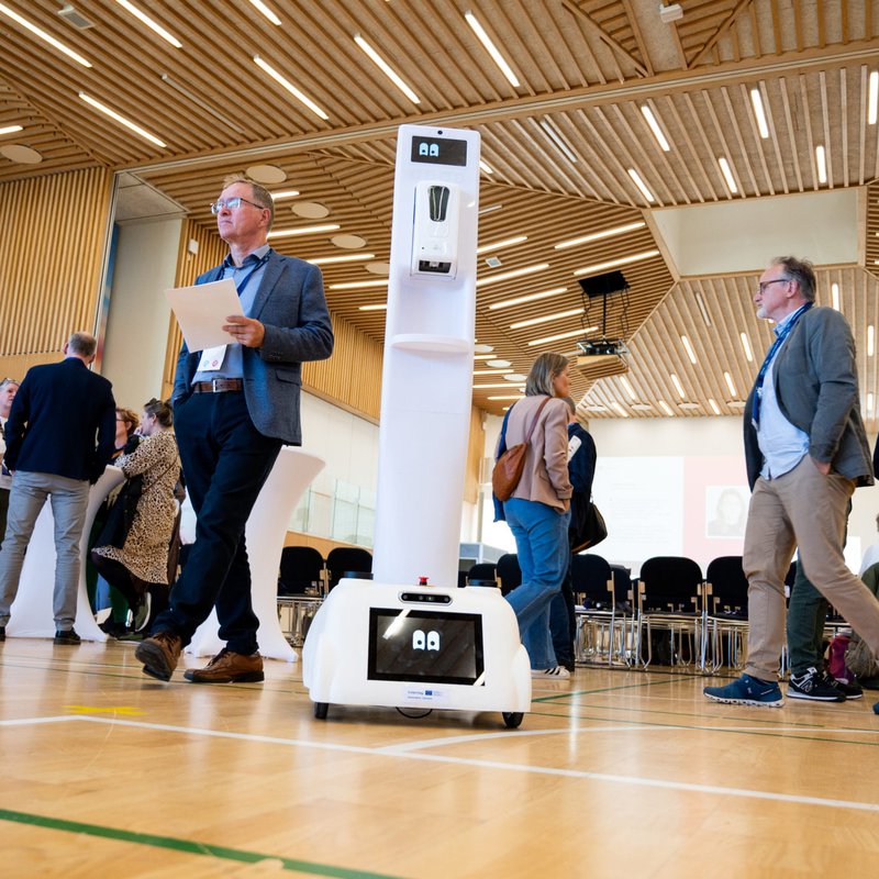 In einem Foyer stehen Menschen in der Mitte ein Roboter.
