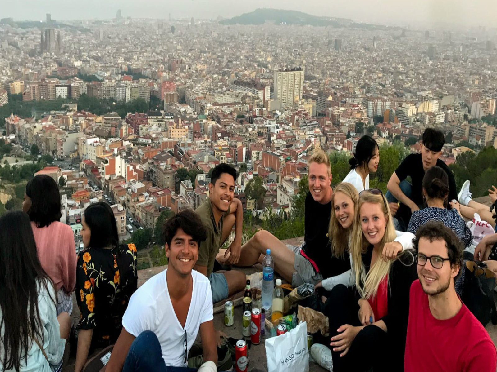 Eine große Gruppe an jungen Menschen sitzt zusammen an einem Platz, von dem aus man über die Dächer der Stadt schauen kann.