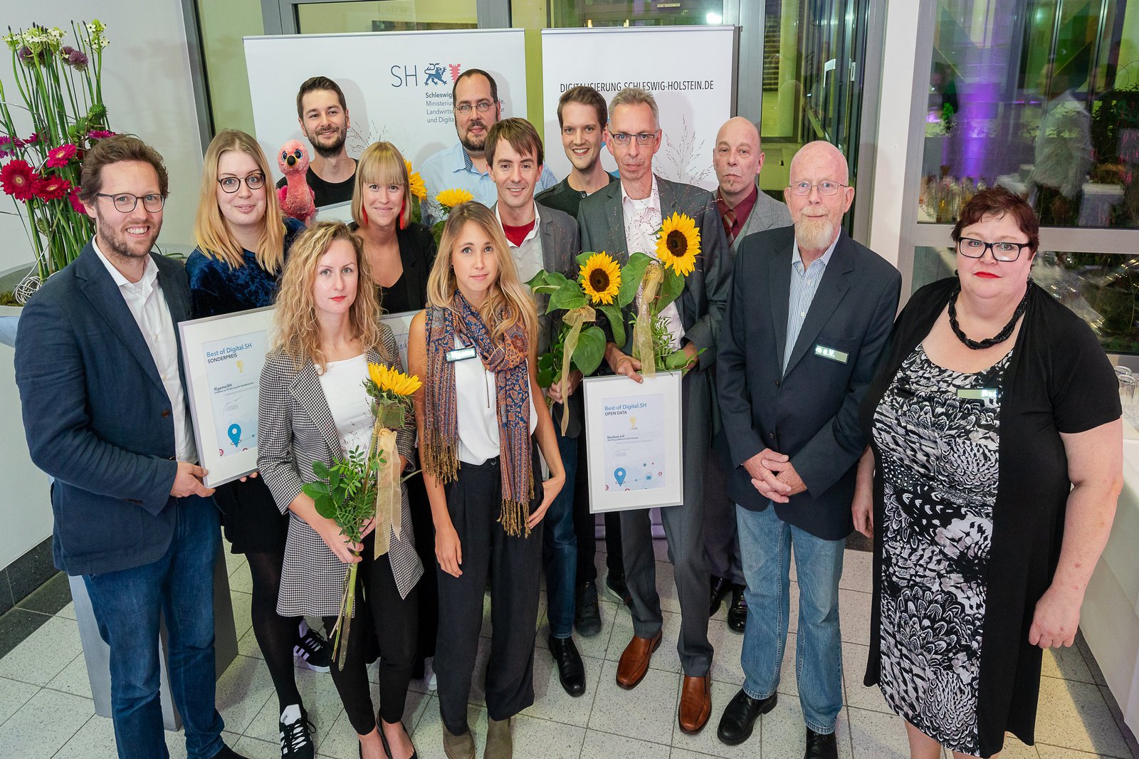 Eine Gruppe Menschen hält Auszeichnungen und Sonnenblumen hoch.