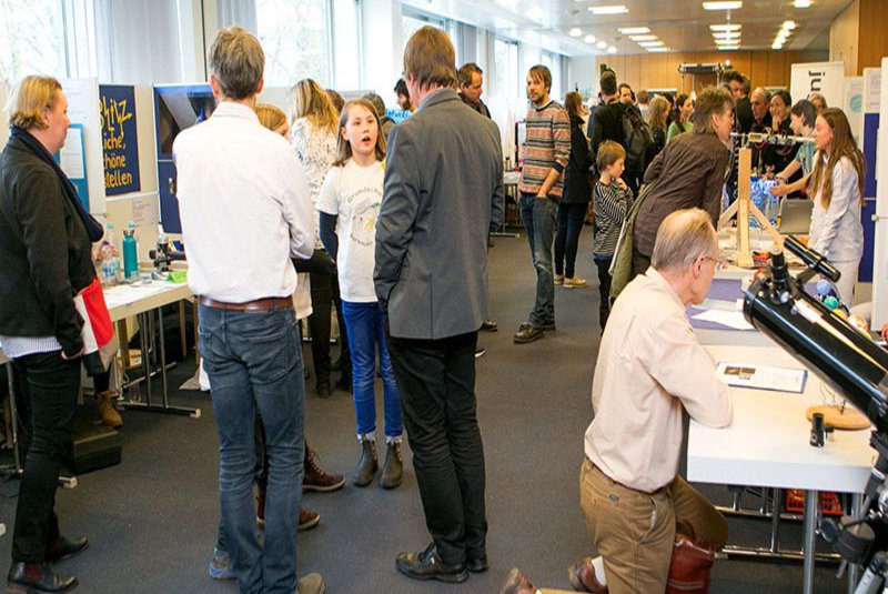 Eine Gruppe Menschen gemischt aus KIndern und erwachsenen schaut interessiert was es an den Infoständen zu erfahren gibt.