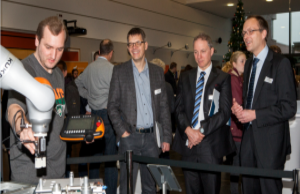 Drei Männer im Anzug schauen sich, aus sicherem Abstand, einen Industrieroboter an.