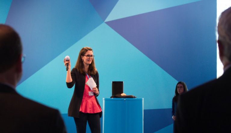 Eine Frau steht auf einer Bühne und hält ihrem Preis in die Höhe.