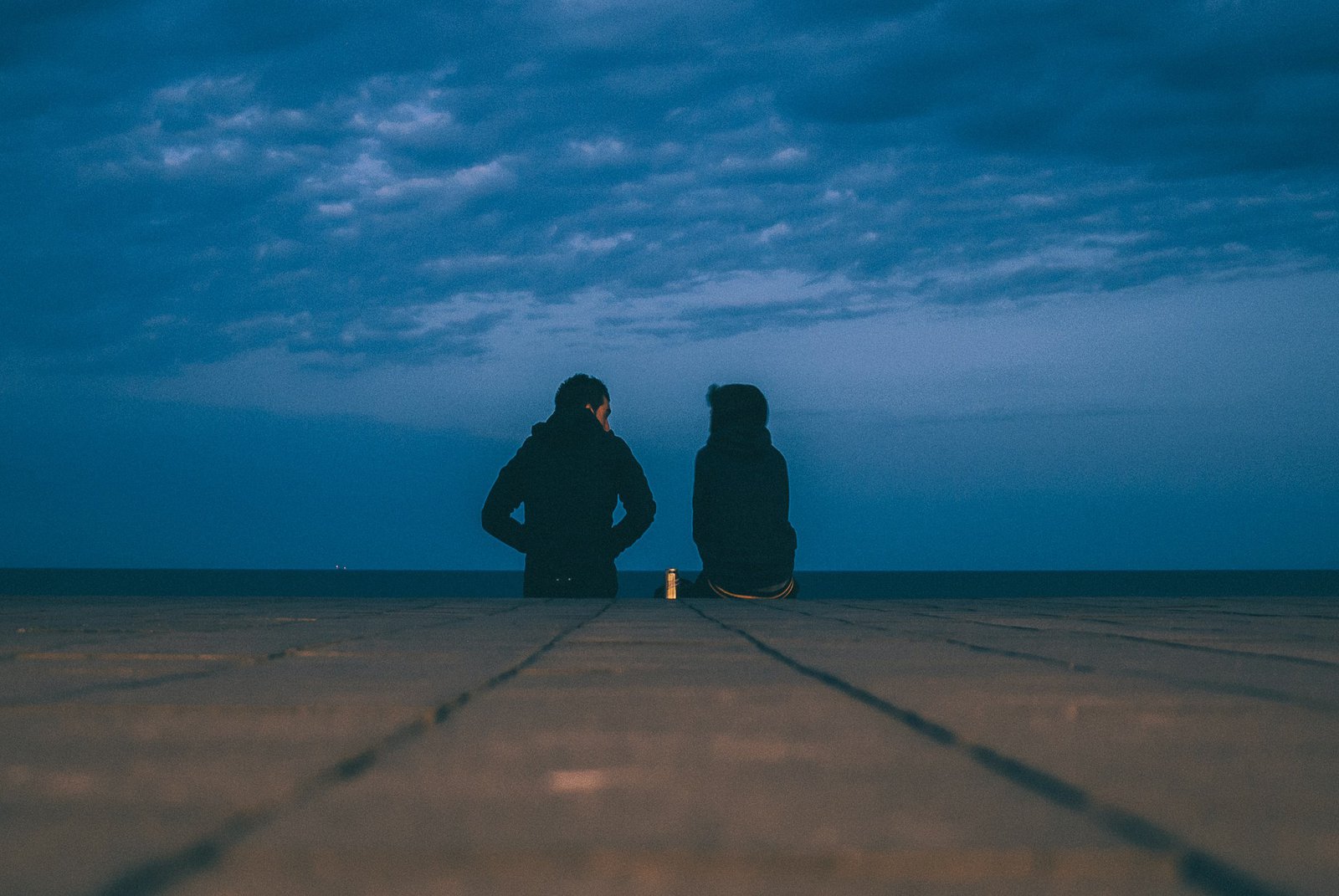 Silhuette zweier nebeneinander sitzender Personen unter blauem Himmel