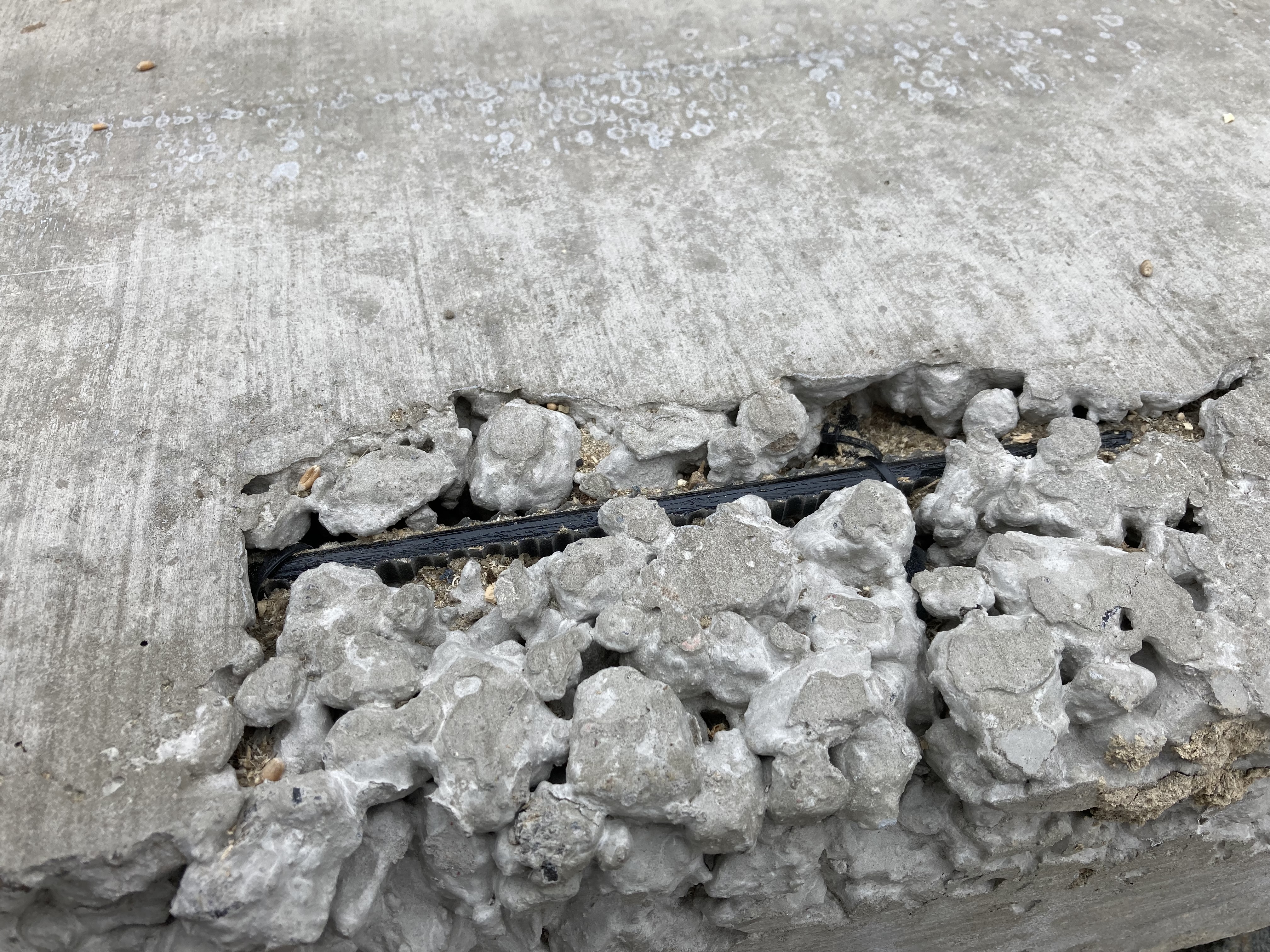 Graue Betonfläche mit grober Struktur, Bewehrungselement aus schwarzer Basaltfaser ist durch die Struktur sichtbar