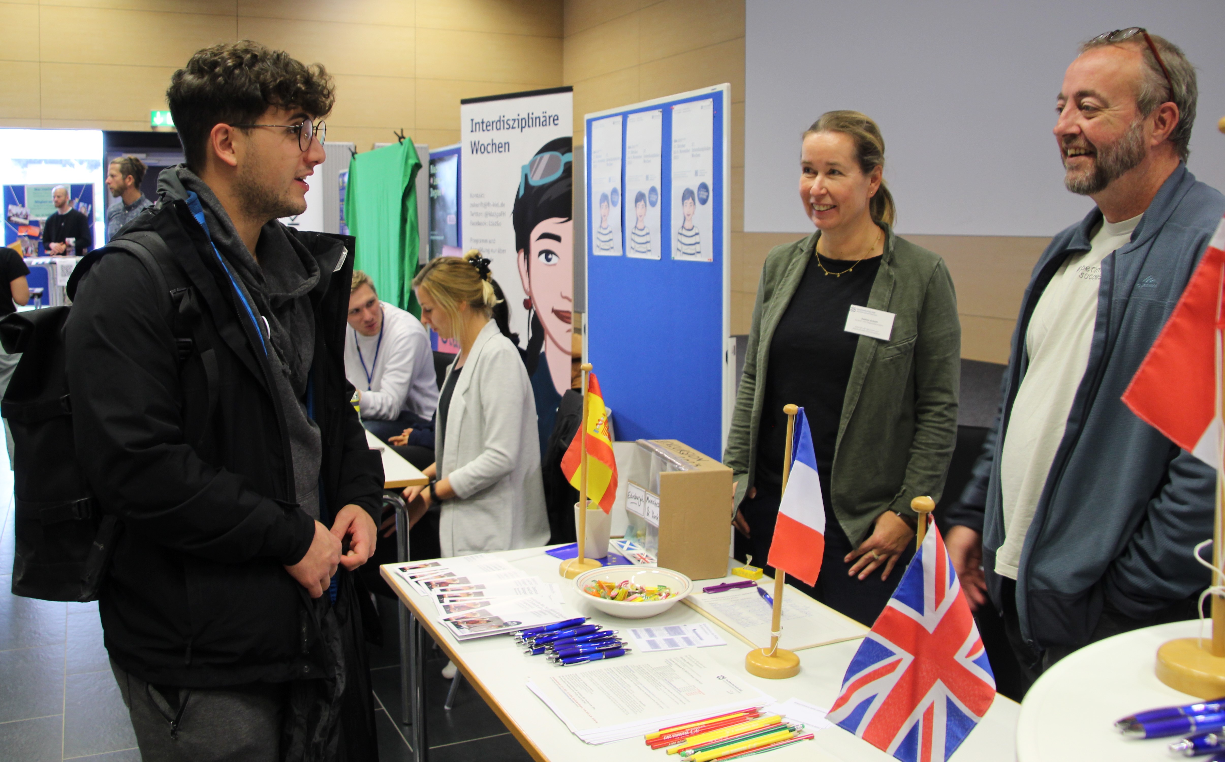 Ein Student im Gespräch mit einer Frau und einem Mann am Messestand