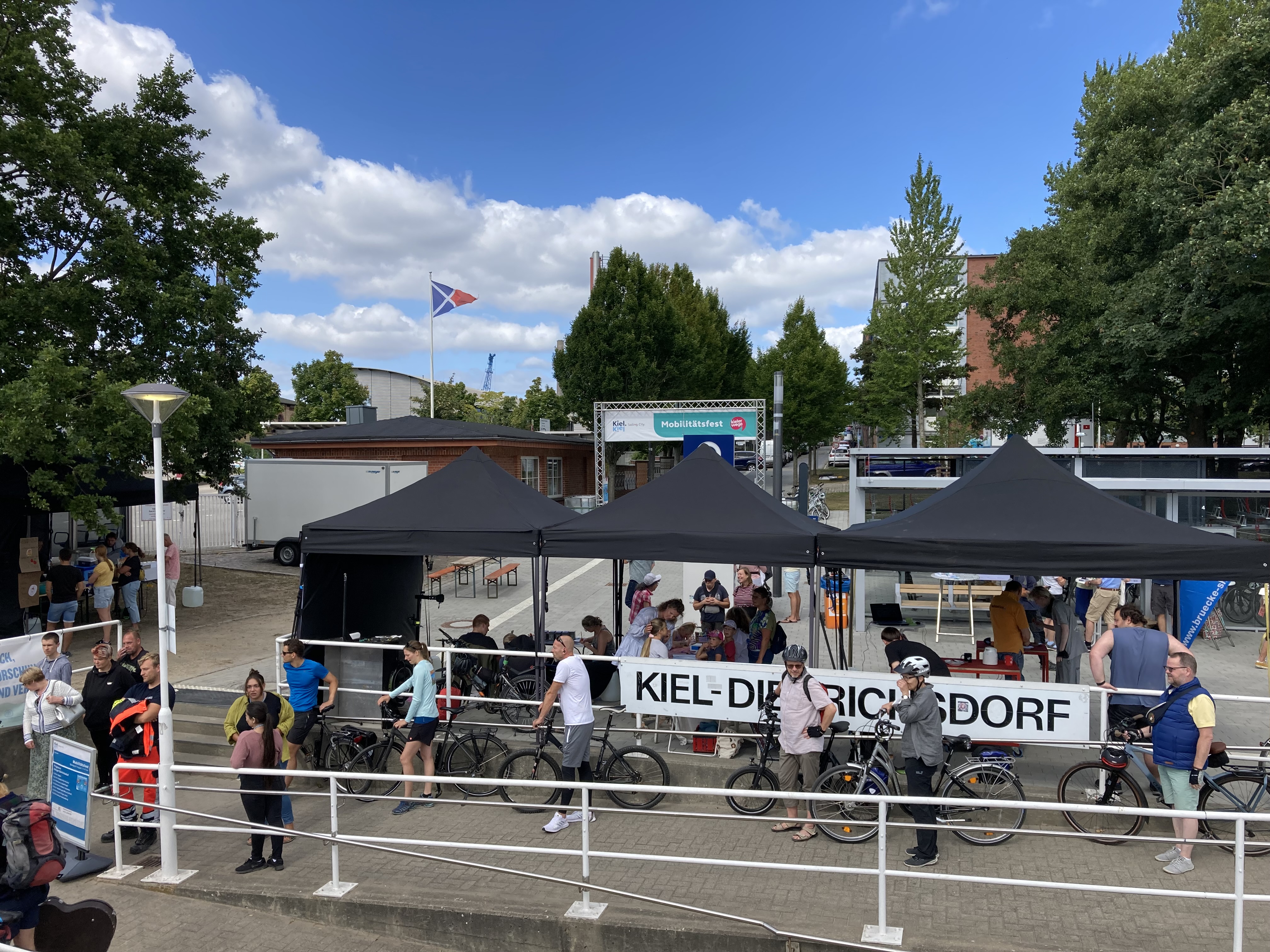 Der Fähranleger Dietrichsdorf von der Fähre aus, im Vordergund wartende Menschen, Hintergrund Pavillons