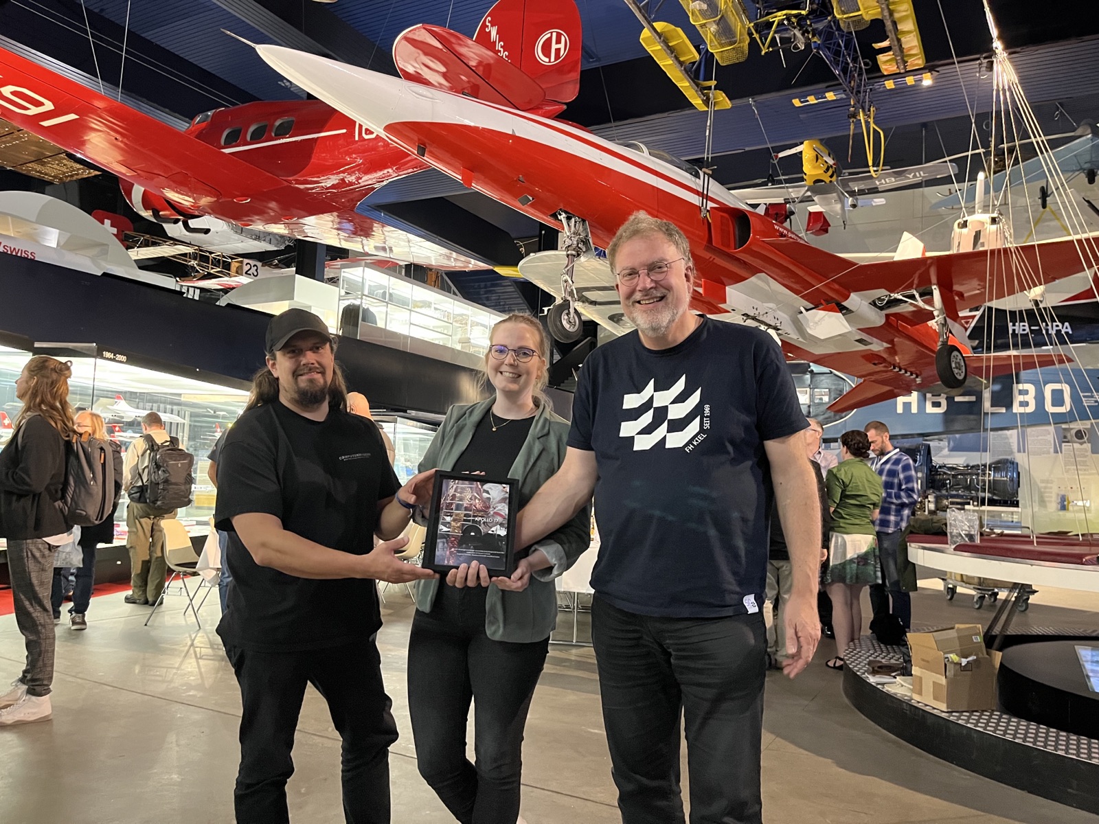 Zwei Männer und eine Frau (Mitte) halten lächelnd eine Auszeichnung in die Kamera