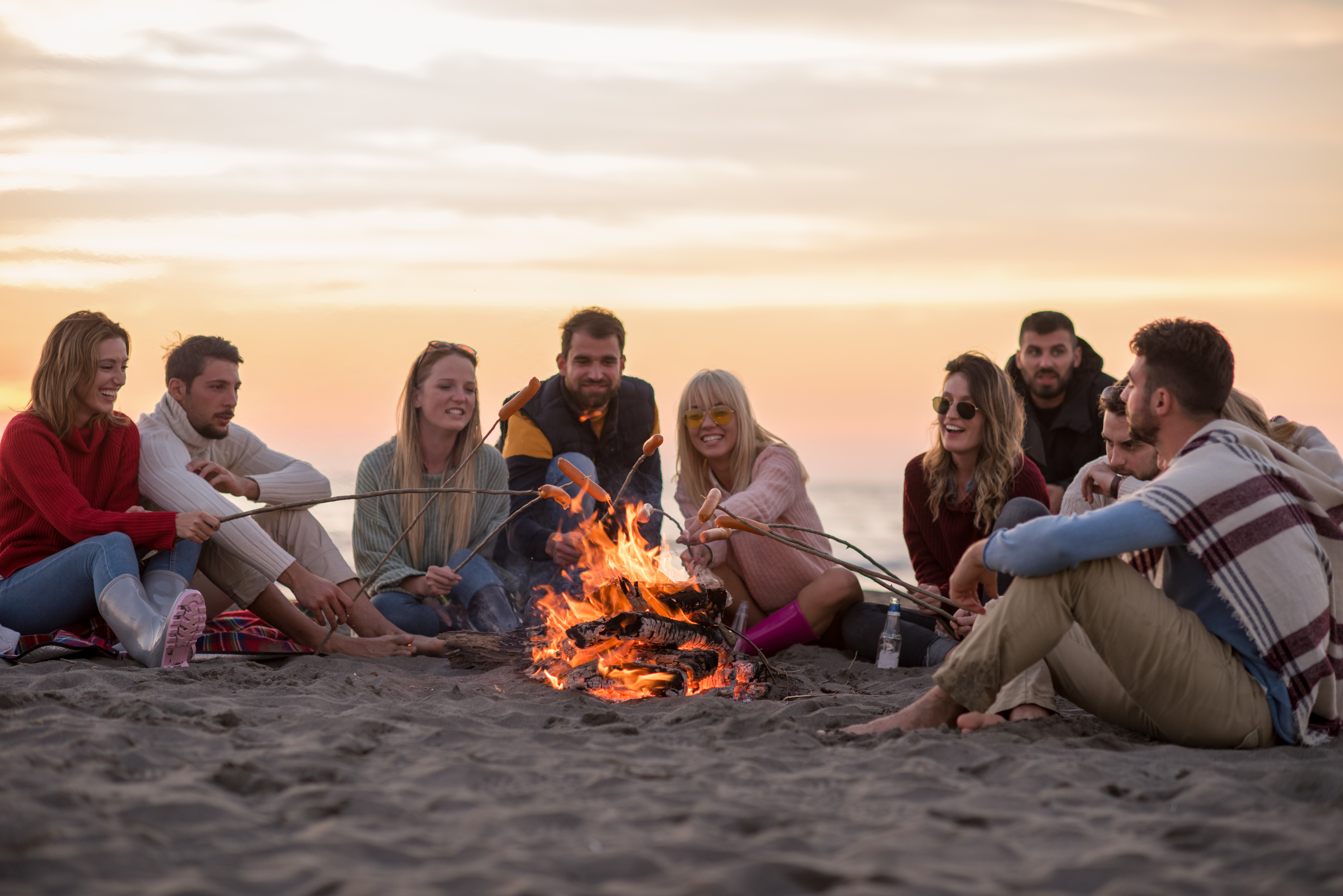 Group Of Young Friends Sitting By The Fire at beach Menschen am Lagerfeuer
