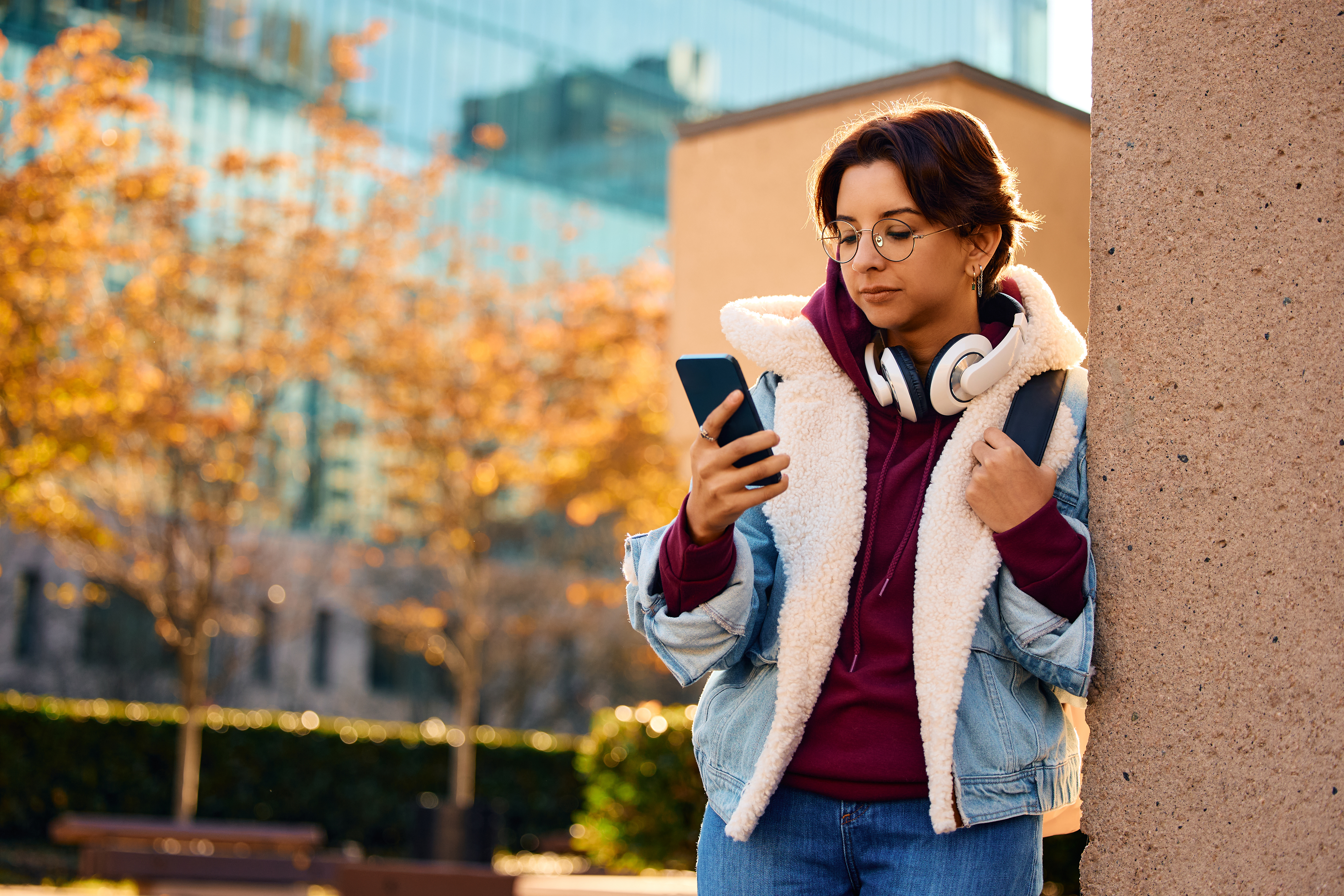 Female university student using mobile phone at campus. eine Studentin mit Smartphone in der Hand lehnt an einer Wand