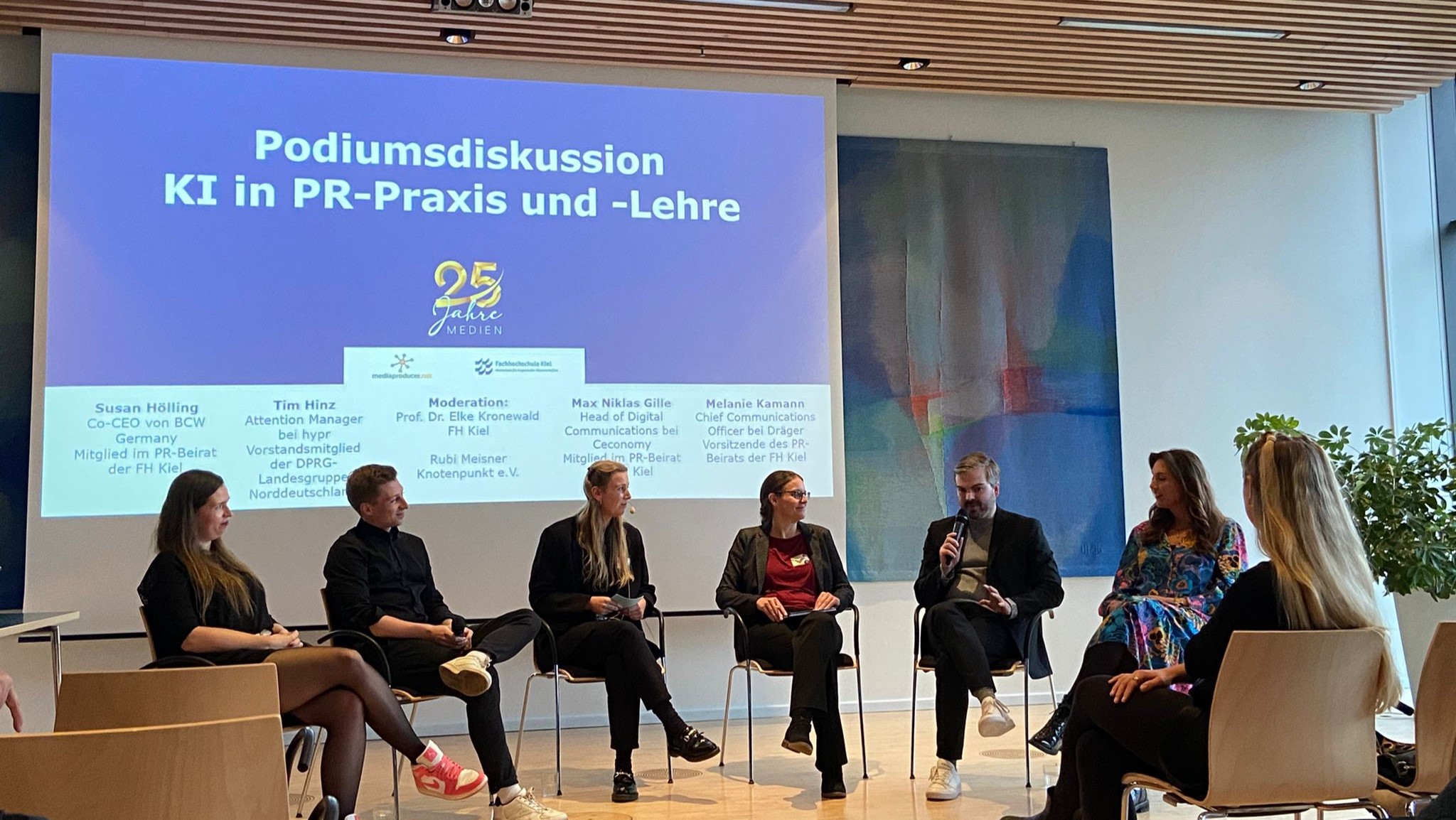 Sechs Personen sitzen auf Stühlen auf einer Bühne