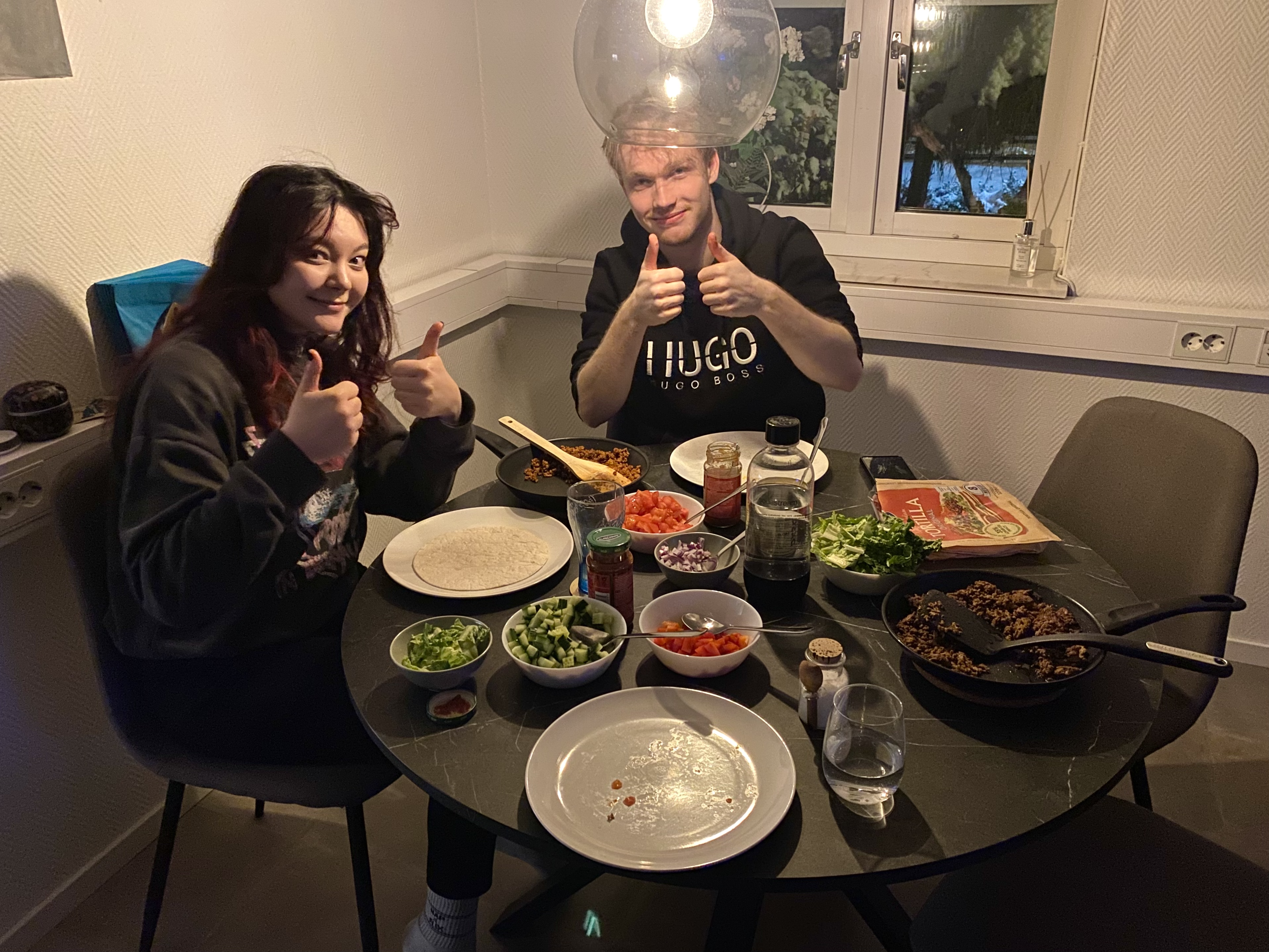 eine Studentin und ein Student sitzen an einem mit Zutaten für Tacos gedeckten Tisch