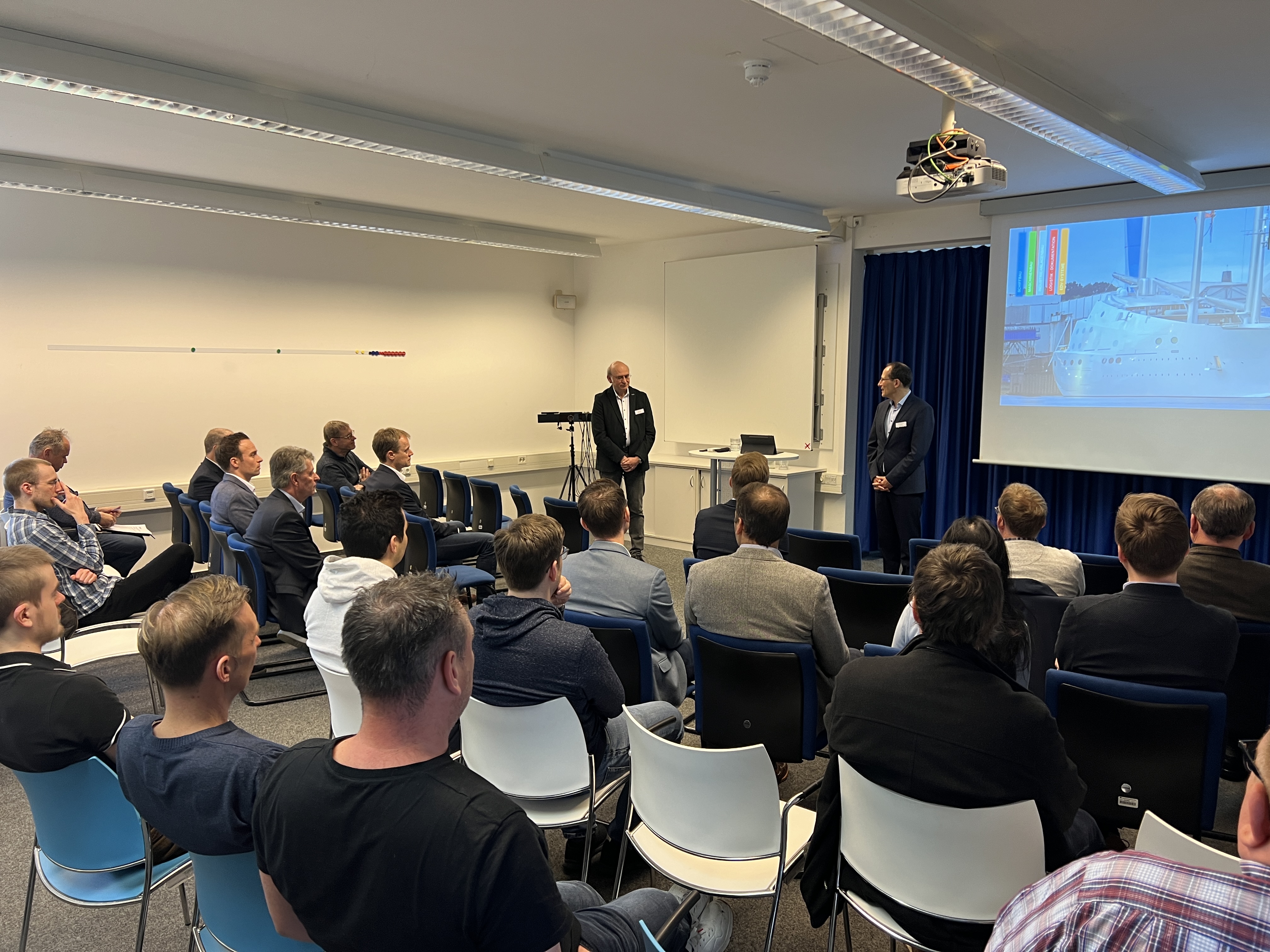 Gäste der Spätschicht in der Digitalen Fabrik der FH Kiel verfolgen in Stuhlreihen sitzend die Einführung ins Thema des Abends