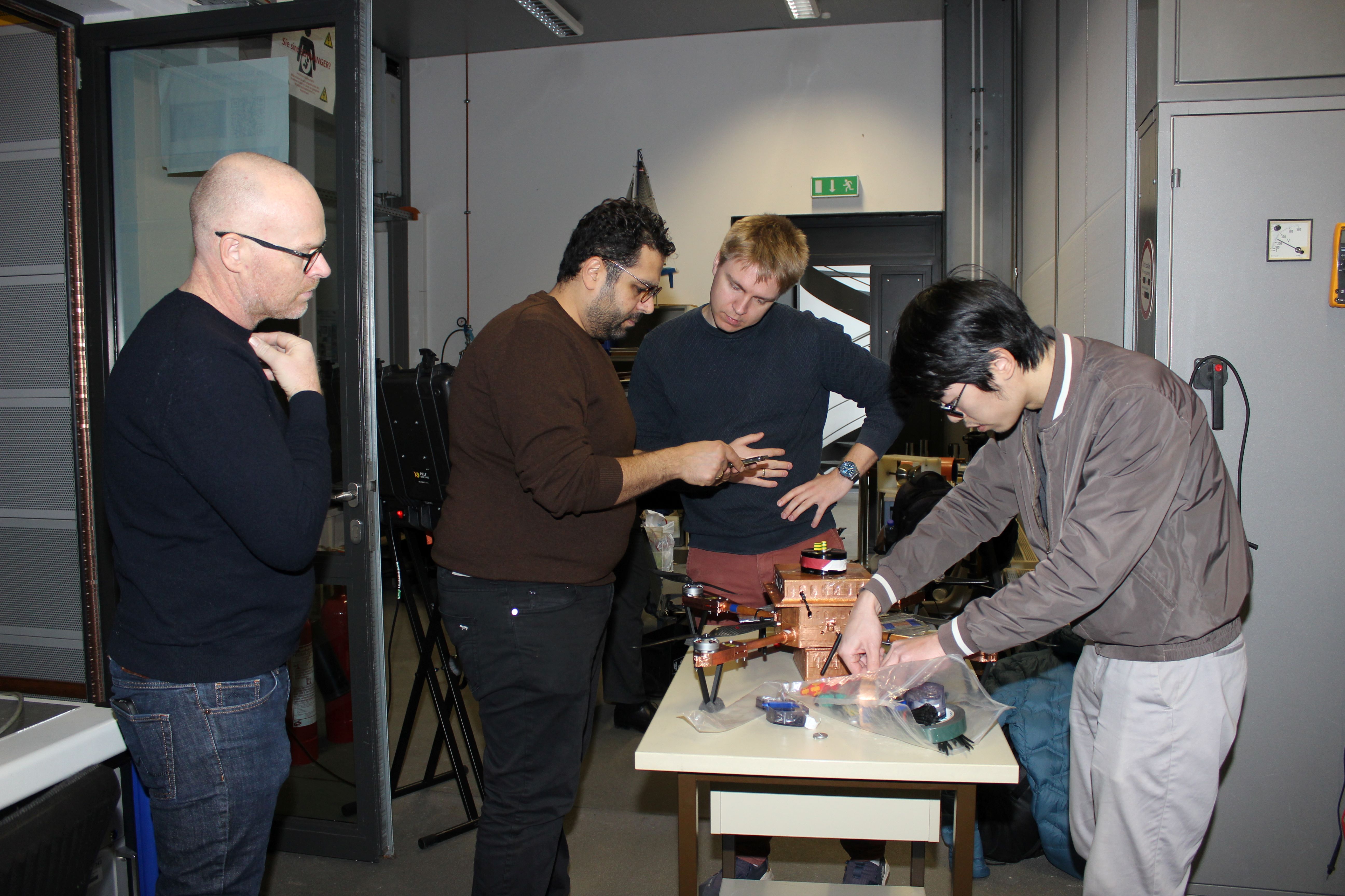 vier Wissenschaftler stehen um einen Tisch herum, auf dem sie eine Drohne für den Test im Blitzlabor der FH Kiel vorbereiten