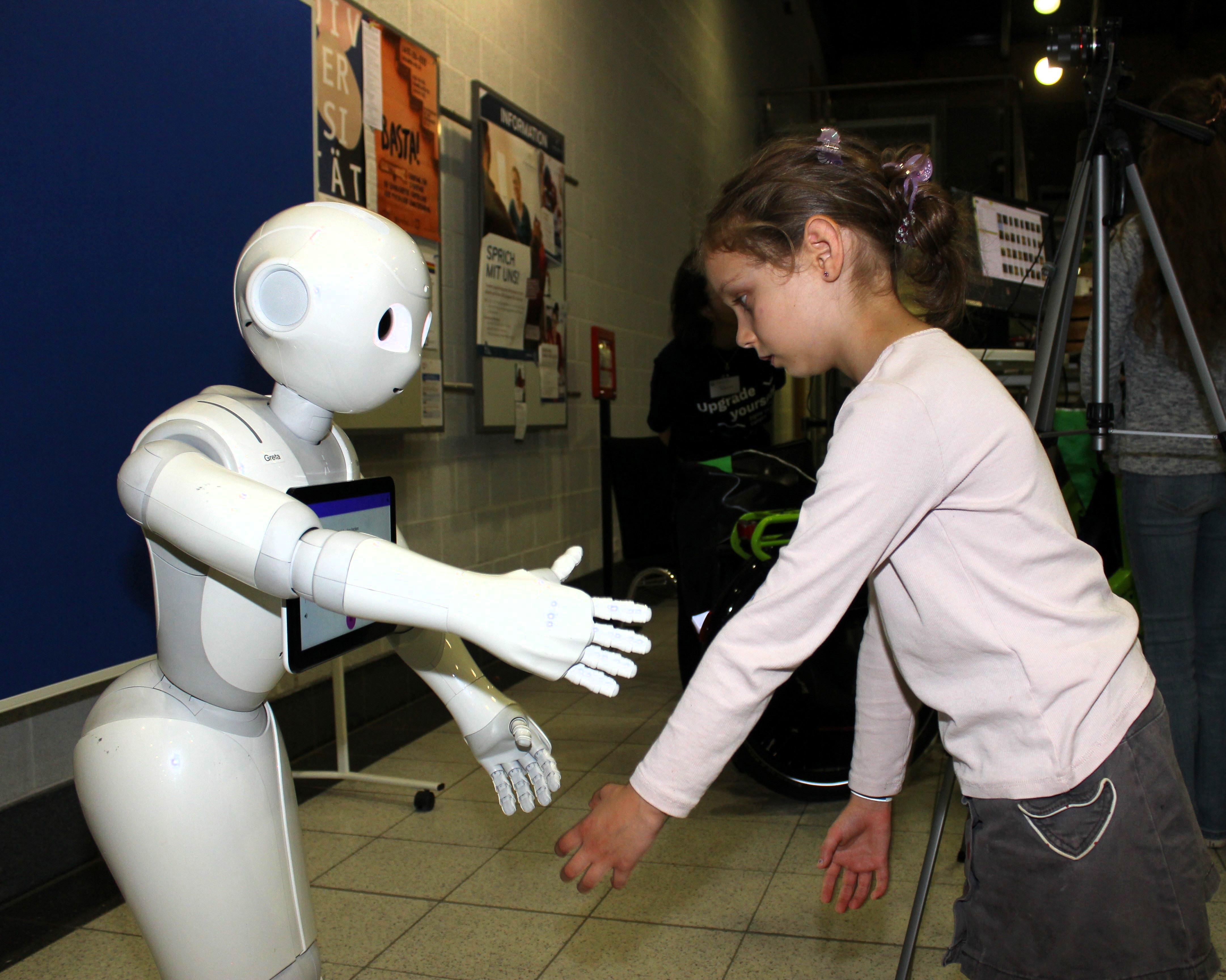 ein Mädchen ahmt einen Roboter nach, der ihr gegenüber steht