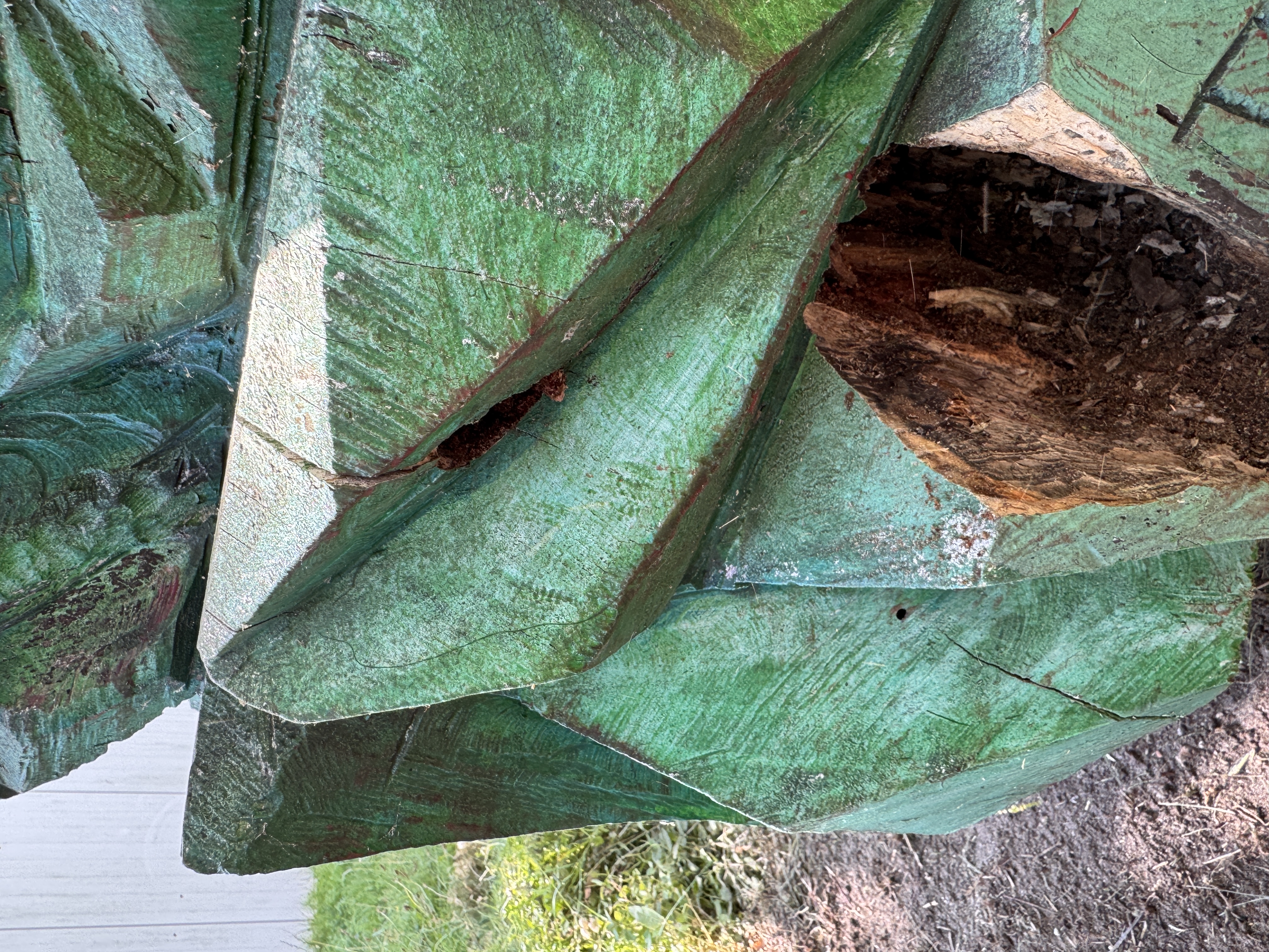 Eine grüne Holzfigur mit einem Loch, das von Insekten gefressen wurde.