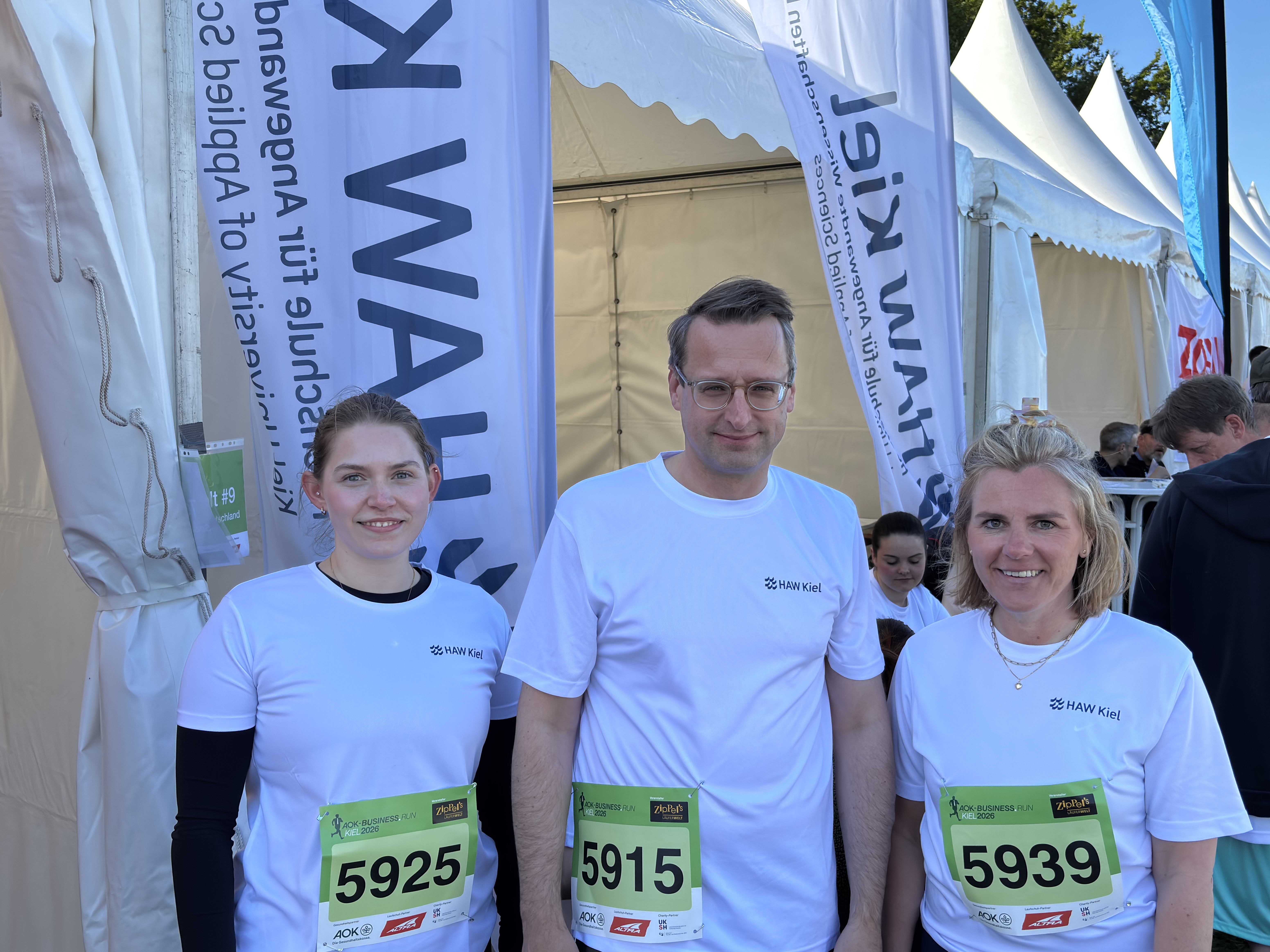 zwei Frauen und ein Mann zwischen bei Beachflags der HAW Kiel beim Business.Run 2026 an der Kiellinie