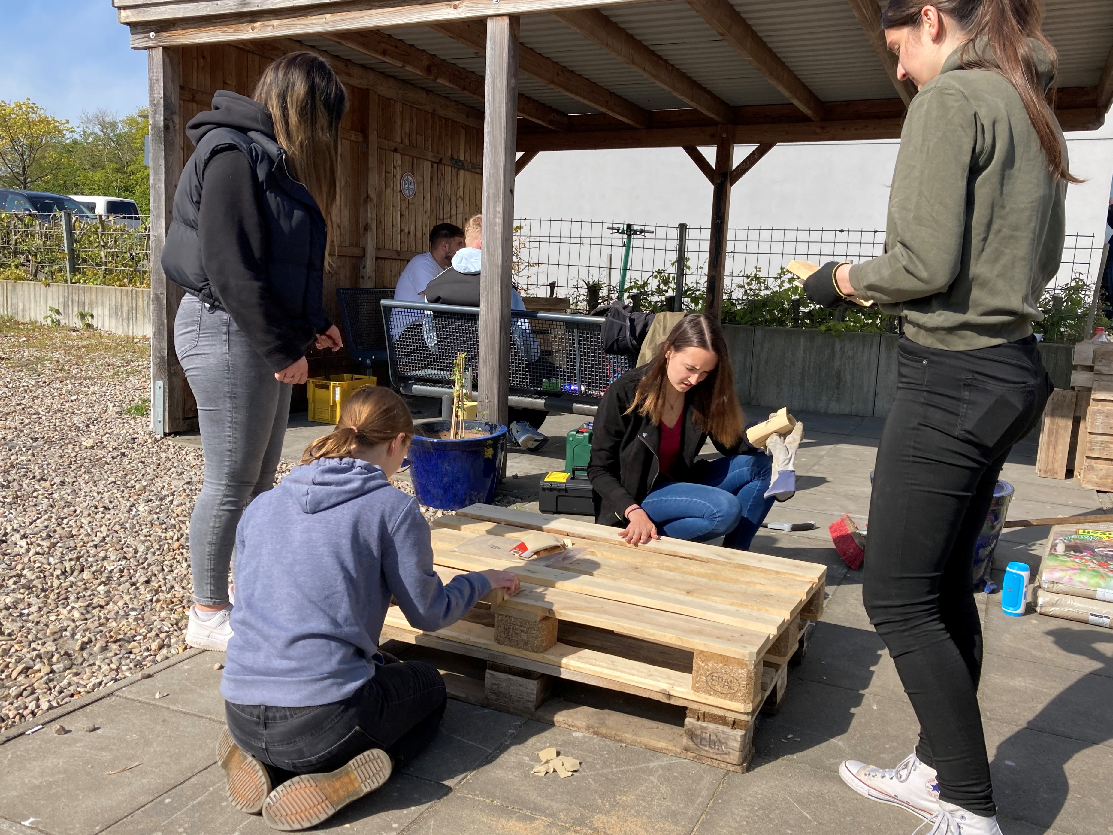 Schüler*innen und Studierende schleifen Europaletten, um daraus Möbel zu bauen