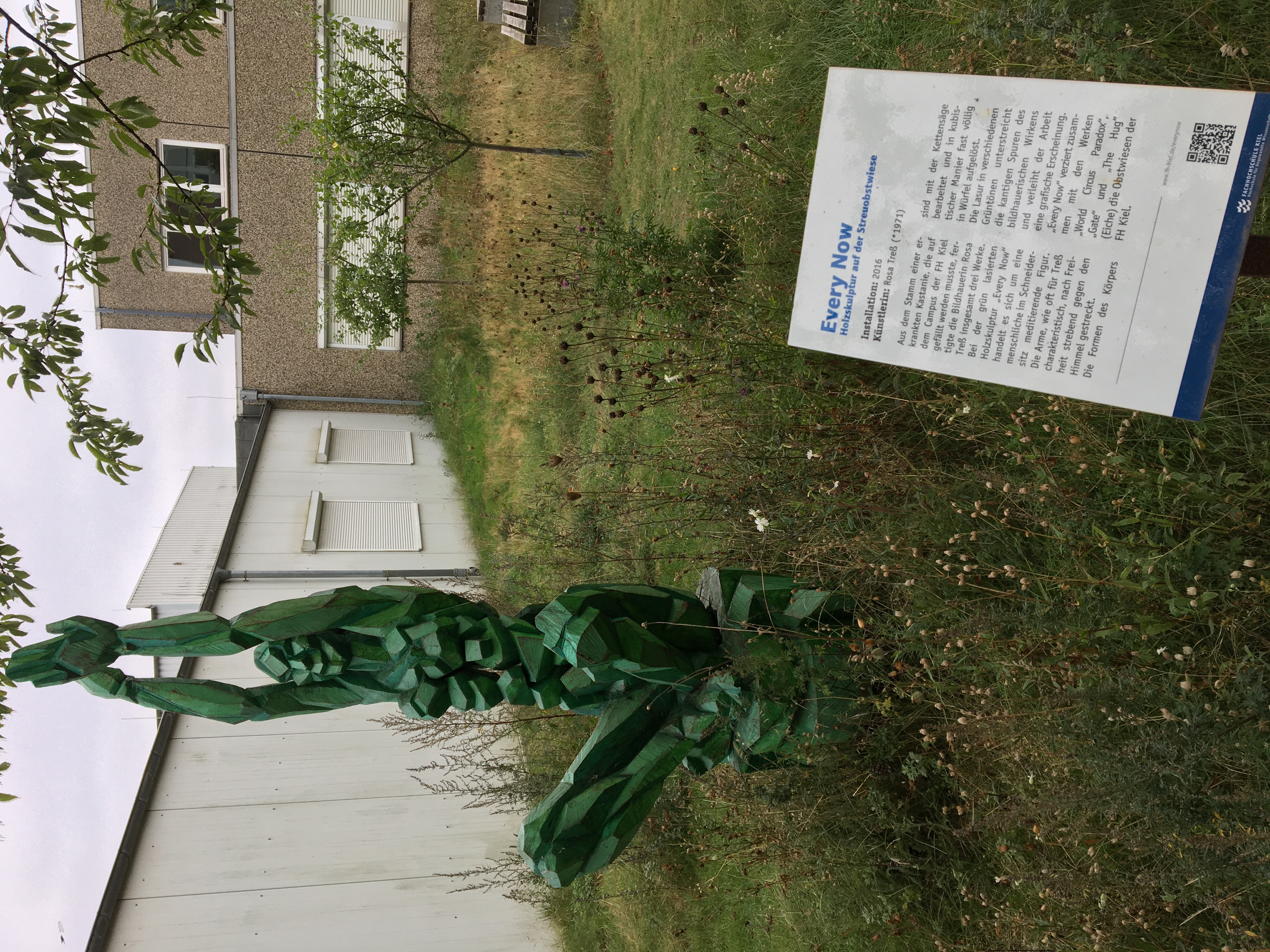 Grüne meditierend sitzende Holzskulptur, die ihre Hände gen Himmel streckt