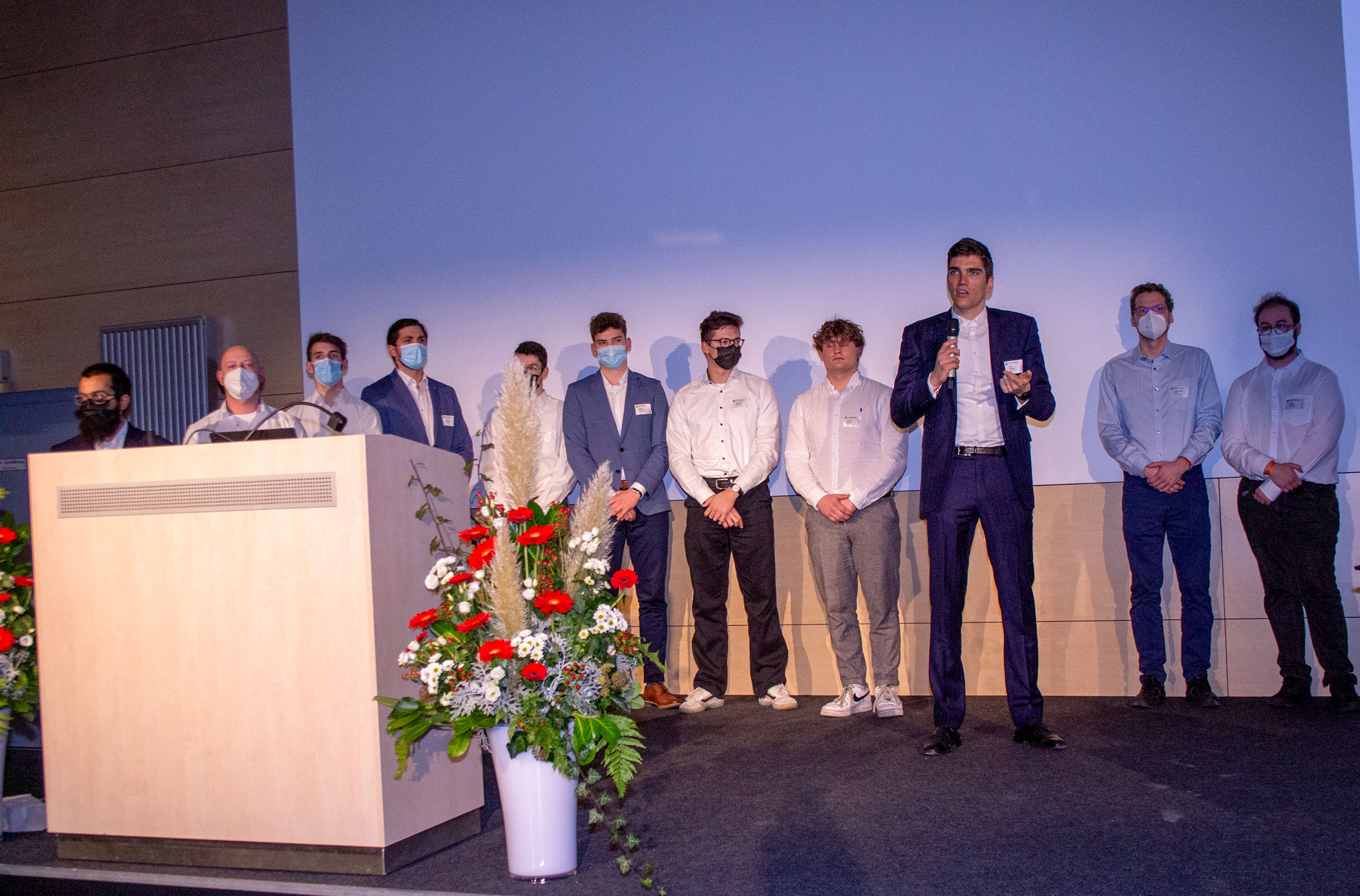 Eine Gruppe junger Männer auf der Bühne hinter einem Rednerpult, einer der Männer hält ein Mikrofon