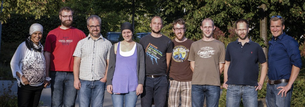 Eine Gruppe aus Männern und Frauen posiert, in einer Reihe, für die Kamera.