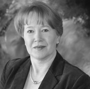 Das Schwarz-Weiß-Bild zeigt eine Frau mit kurzen Haaren, die ein Jackett und eine Perlenkette trägt.