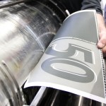 Eine Hand entnimmt einen Druck, von der Druckerwalze.