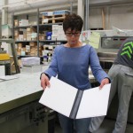 Eine Frau hält einen Druck in die Kamera.