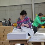 Eine Frau bearbeitet einen dicken Stapel fertiger Drucke.