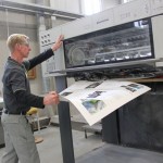 Ein Mann entnimmt einen Fetigen Druckbogen aus der Druckerpresse.