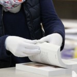 Zwei mit Handschuhen bekleidete Hände, gehen das fertige Druckwerk noch einmal durch.