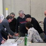 Eine Gruppe Männer und eine Frau stehen beratschlagend um einen Tisch herum.