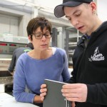 Ein Mann hält das fertige Buch in den Händen. Neben ihm steht eine Frau, welche dieses noch einmal kritisch begutachtet.