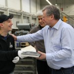 Ein älterer Mann in Hemd, klopft einem jüngeren mit cap wertschätzend auf die Schulter.