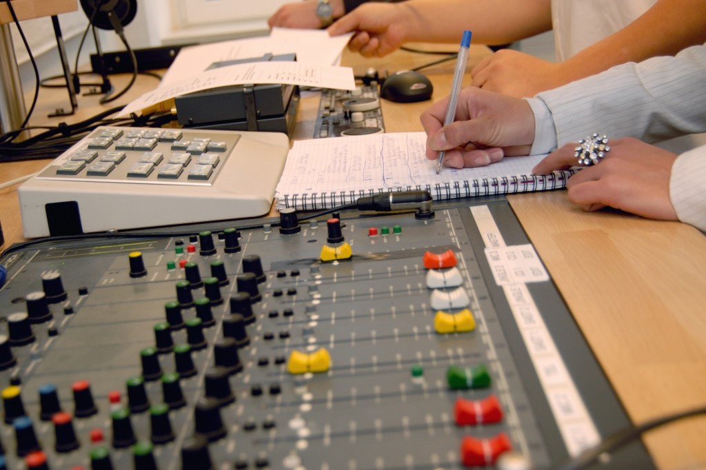 Neben einem Mischpult machen mehrere Händepaare Notizen.