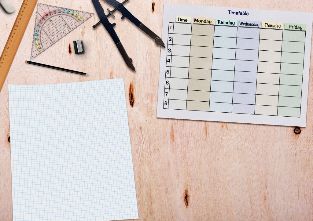 Auf einem hellen Holztisch liegt ein Stundenplan und mehrere Zeichenwerkzeuge.
