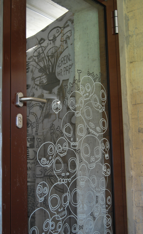 Auf einer gläsernen Eingangstür sind viele Totenköpfe zu sehen.