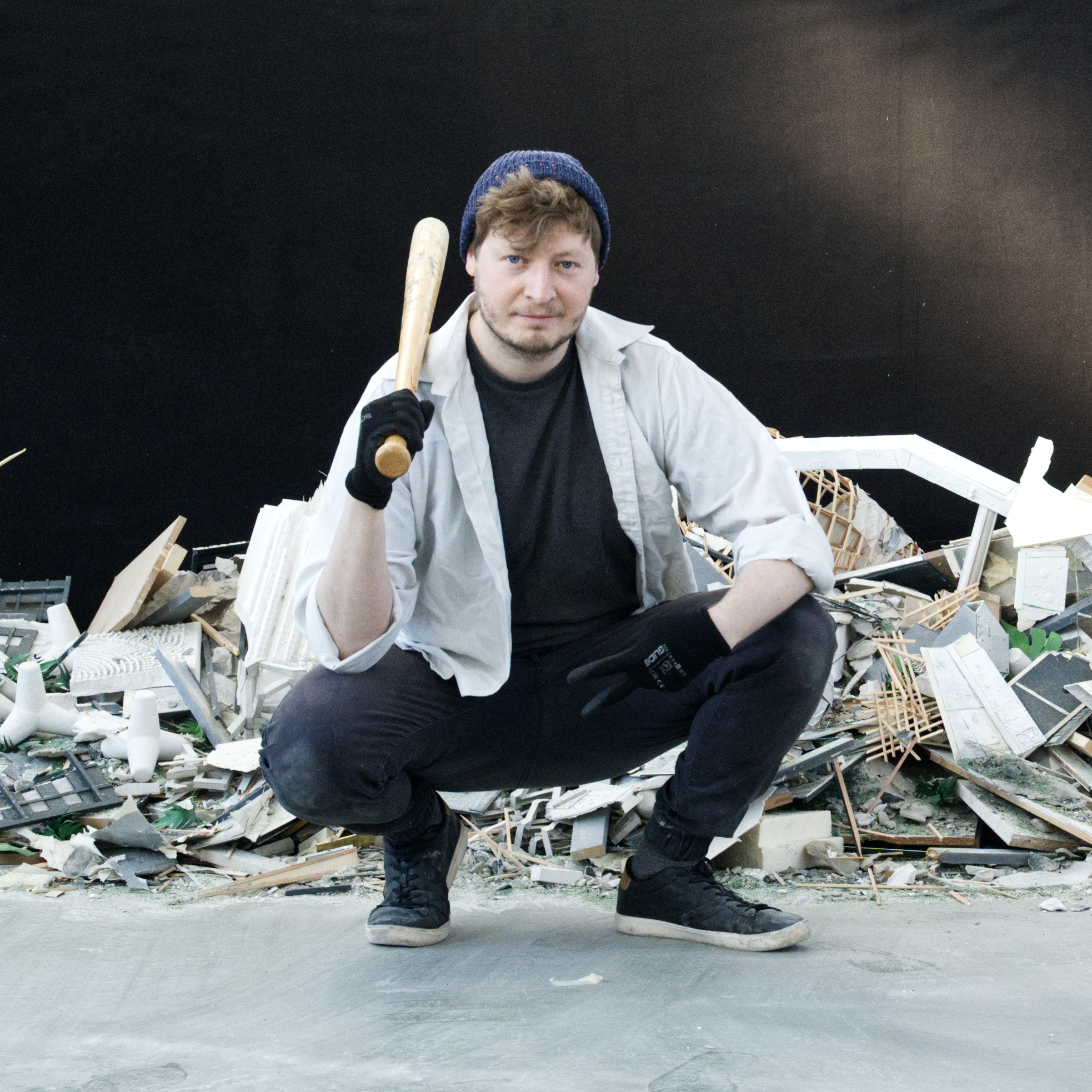 Ein junger Mann mit Basecap hockt, einen Baseballschläger in der Hand, vor einem Haufen zerschlagener Gegenstände