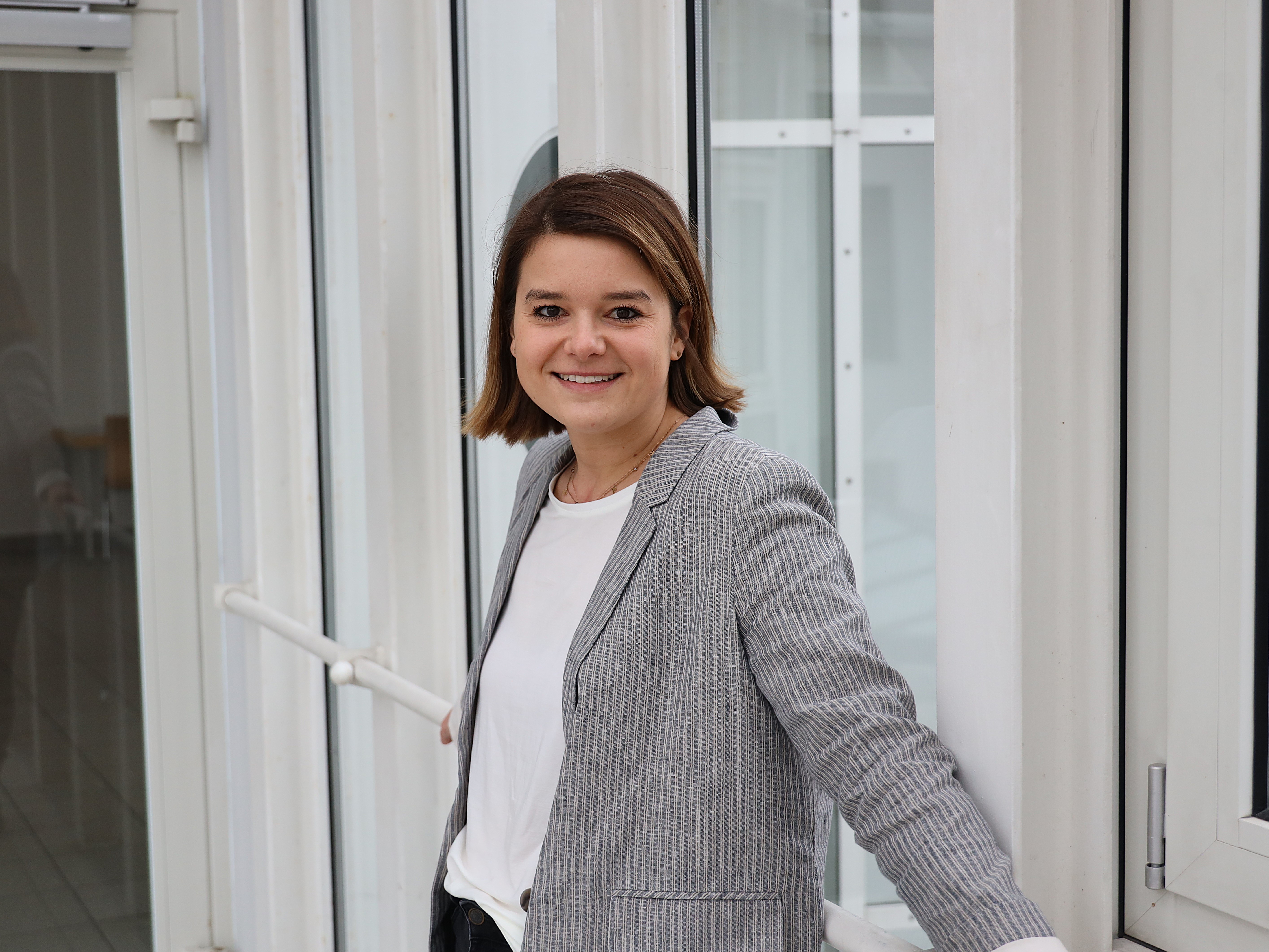 Eine junge Frau steht vor einer Fensterfront. Prof.in Dr.in Monique Ritter ist Professorin für Gender und Soziale Arbeit an der Hochschule Landshut.