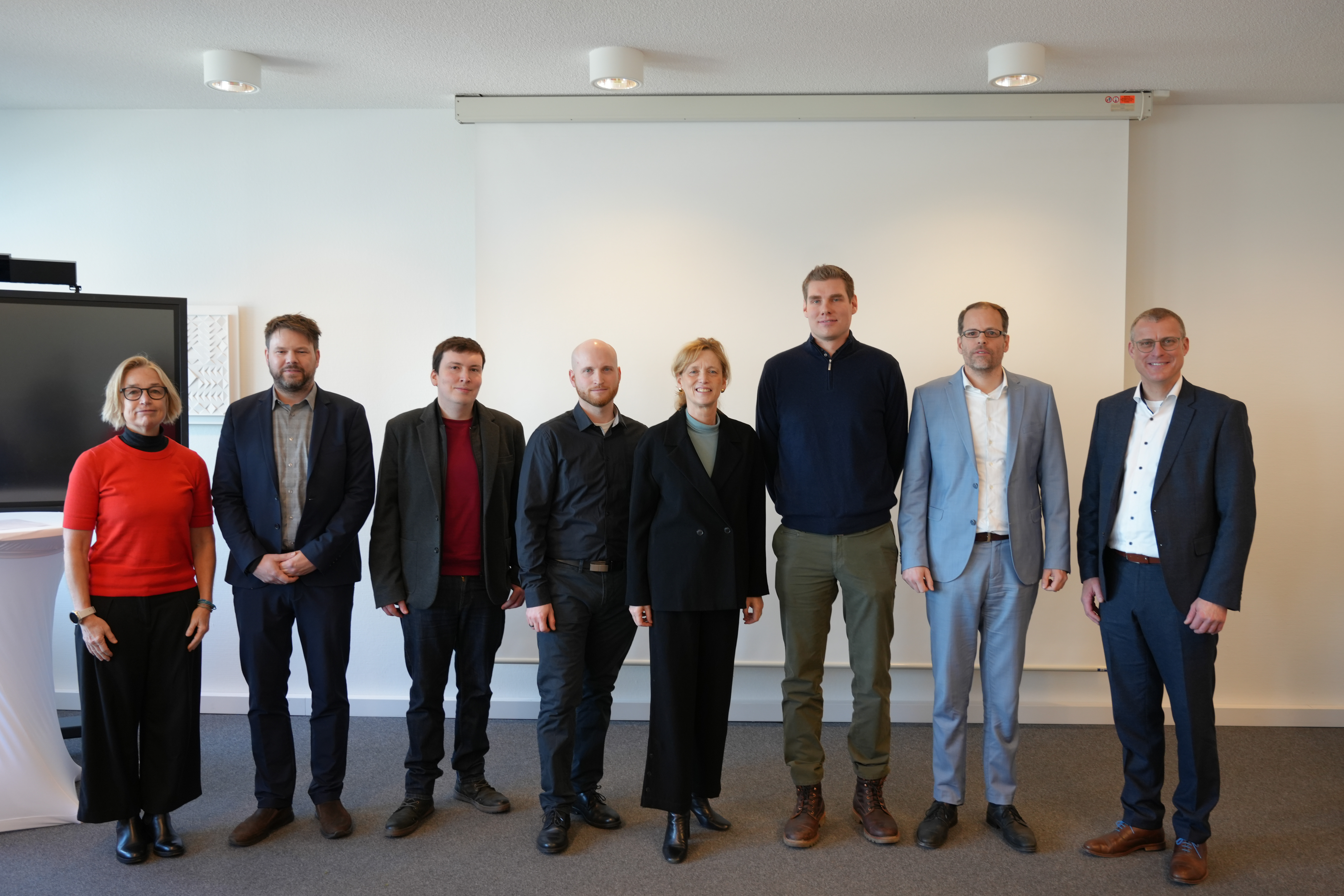 Auf dem Bild sind die in der Bildunterschrift genannten Personen zu sehen. Sie stehen in einer Reihe und lächeln in die Kamera.