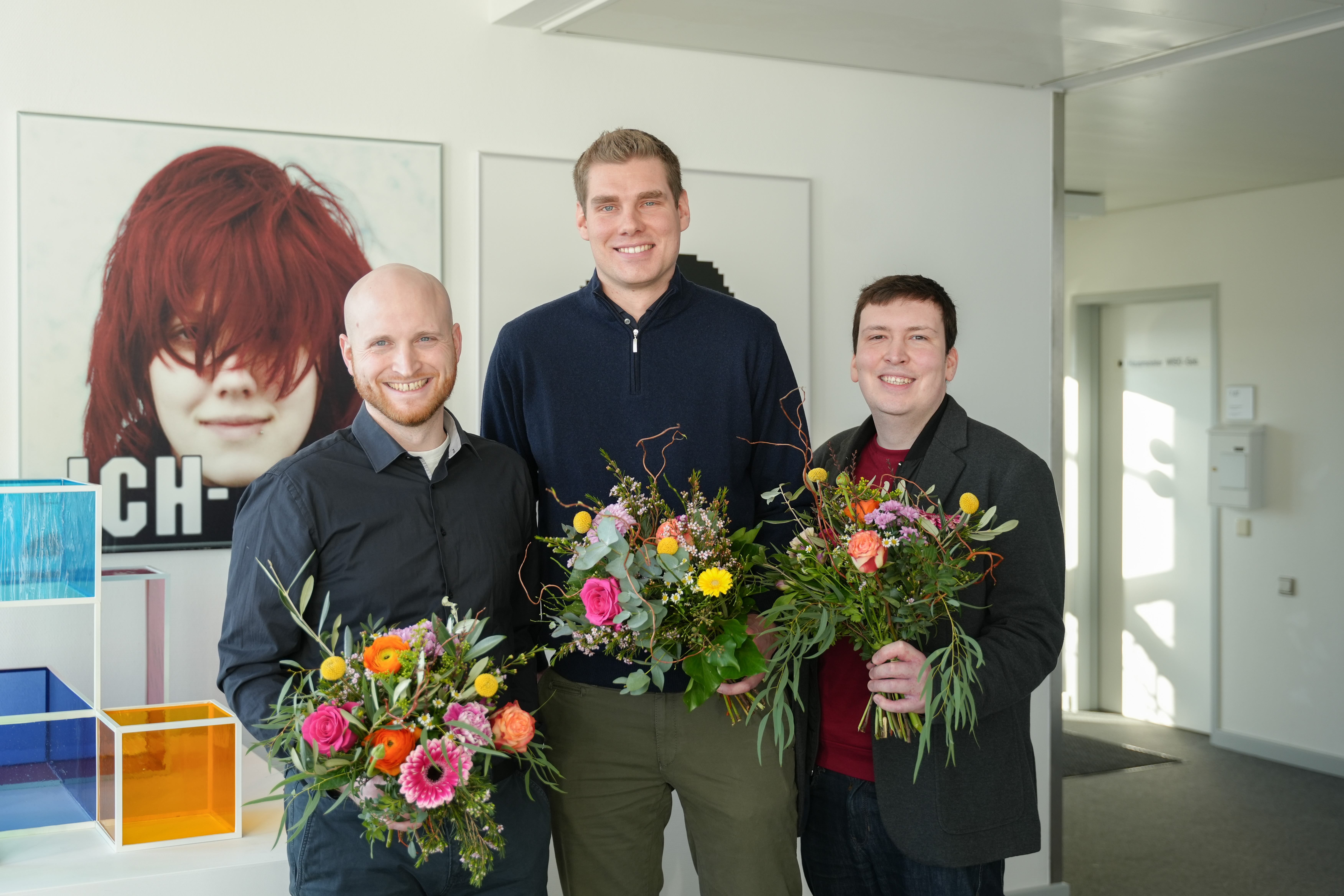 Auf dem Bild sind in einer Reihe Henner Bendig, Niklas Pelka und Ruben Schlonsak zu sehen. Sie halten jeweils einen Blumenstrauß in der Hand und lächeln in die Kamera.